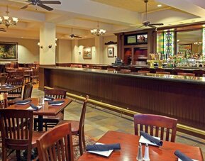 Restaurant and bar area with wooden tables, upholstered seating, and stained glass accents at Hilton Boston Logan Airport.