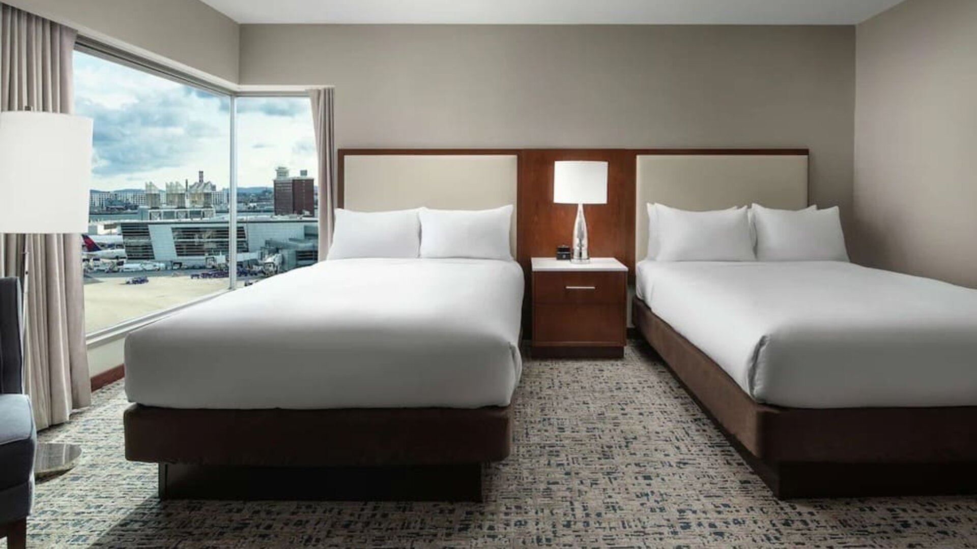 Guest room with two beds and large corner windows overlooking airport and city views at Hilton Boston Logan Airport.