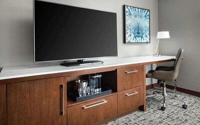 Workspace with desk chair, large TV, coffee station, and wooden cabinetry at Hilton Boston Logan Airport.