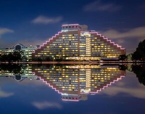 Exterior nighttime view of Hyatt Regency Boston/Cambridge with illuminated pyramid-style architecture reflected on the riverfront.