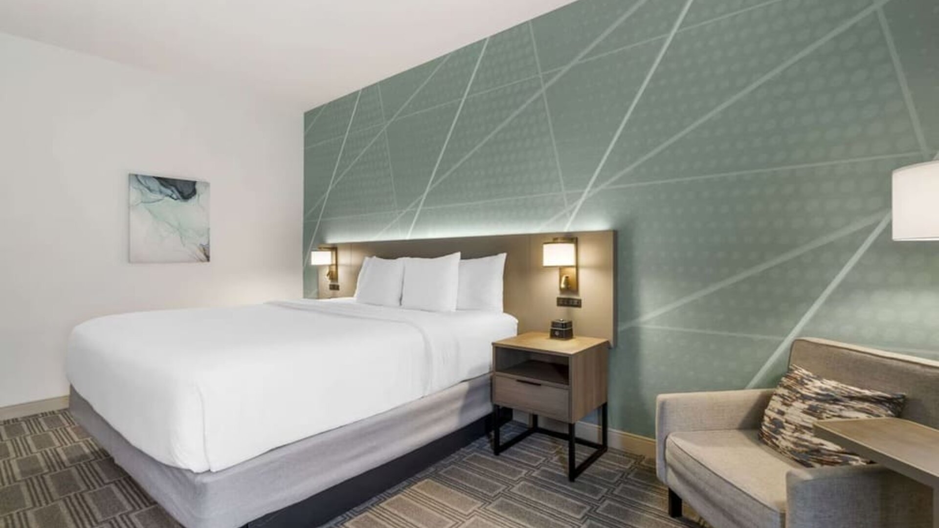 Stylish king guest room with accent wall, plush bedding, and comfortable armchair at Comfort Inn & Suites Port Charlotte-Punta Gorda.
