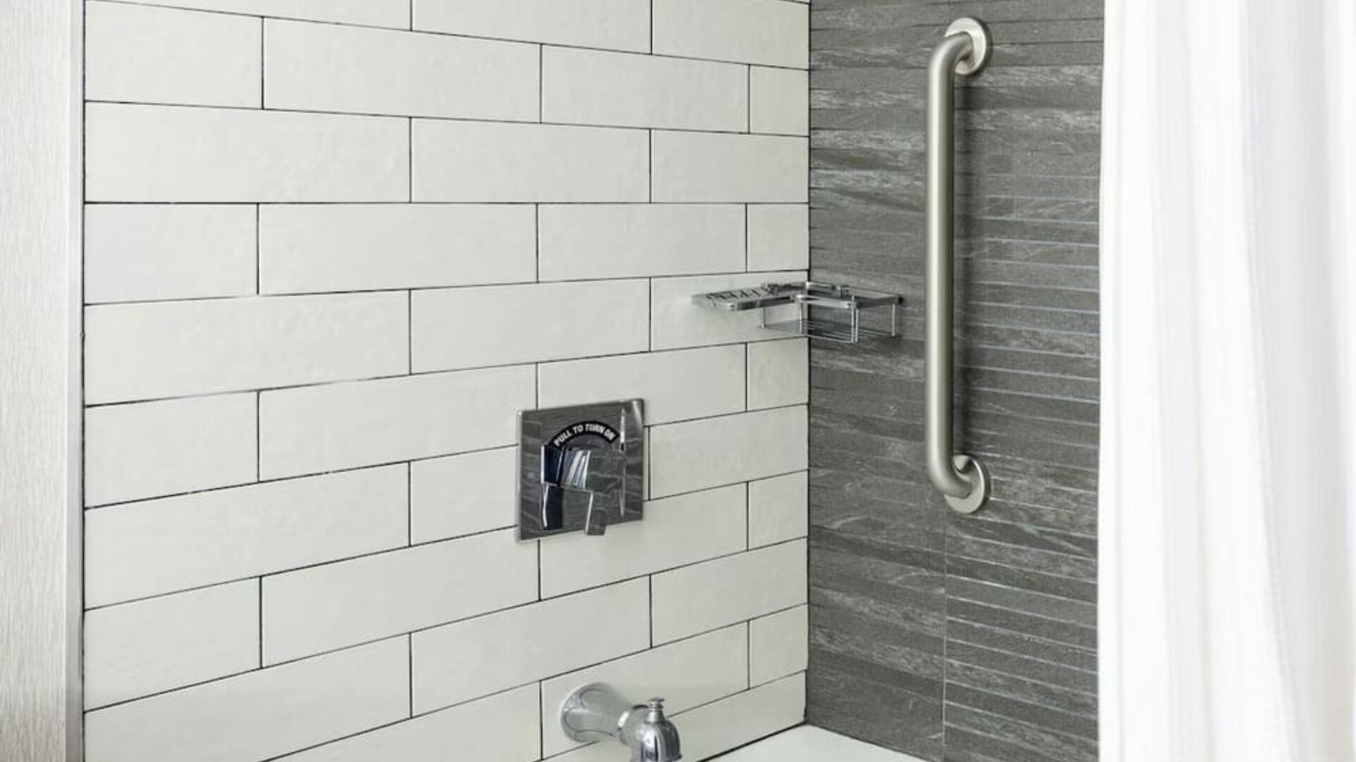 Stylish bathroom with tiled bathtub and rainfall shower fixture featuring sleek modern design at Boston Marriott Newton.