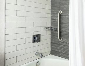 Stylish bathroom with tiled bathtub and rainfall shower fixture featuring sleek modern design at Boston Marriott Newton.