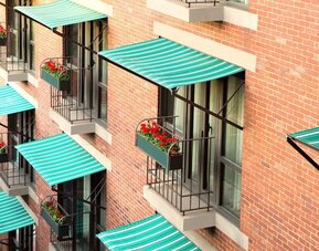 Exterior detail of The Bostonian Boston, A Millennium Hotel featuring charming balconies with striped awnings and flower boxes overlooking the city.