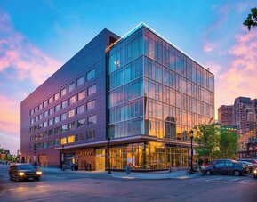 Modern glass-front hotel exterior at sunset showcasing contemporary architecture in Boston’s Seaport District at The Envoy Hotel, Autograph Collection.