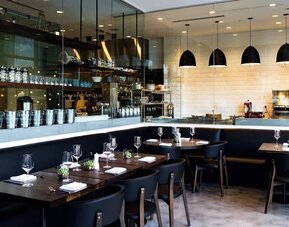 Chic restaurant dining area with open kitchen concept, elegant lighting, and contemporary seating at The Envoy Hotel, Autograph Collection.