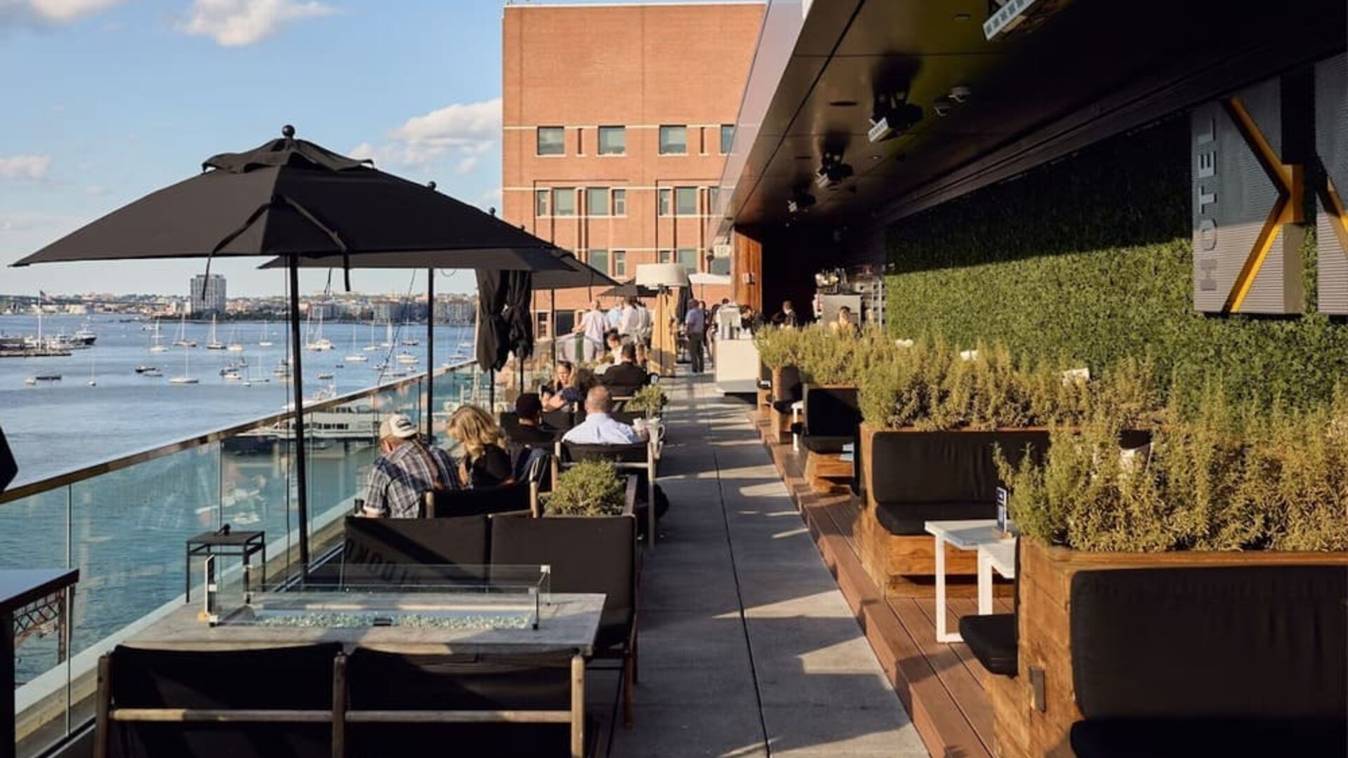 Rooftop outdoor dining terrace overlooking Boston Harbor with lounge seating and scenic waterfront views at The Envoy Hotel, Autograph Collection.