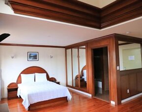 Large king guest suite with polished wood finishes, mirrored wardrobes, and elegant ceiling detailing at Phoenix Hotel Brooklyn Sunset Park.