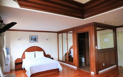 Large king guest suite with polished wood finishes, mirrored wardrobes, and elegant ceiling detailing at Phoenix Hotel Brooklyn Sunset Park.