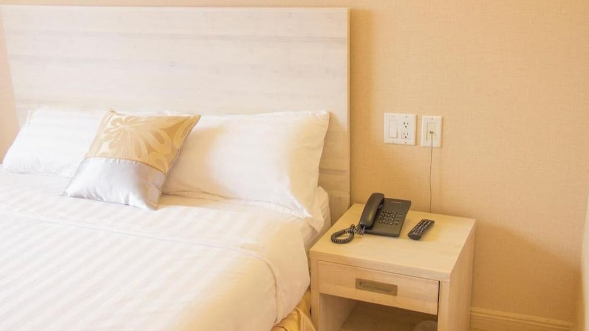 Close-up of a neatly styled guest bed and bedside table with in-room telephone amenities at Phoenix Hotel Brooklyn Sunset Park.