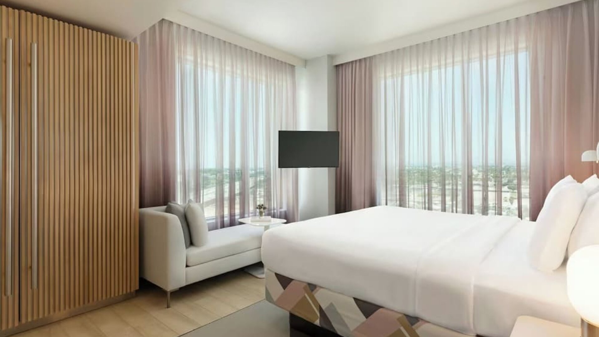 Bright guest room with a king-size bed, floor-to-ceiling windows, comfortable seating area, and panoramic views of the surrounding Anaheim area.