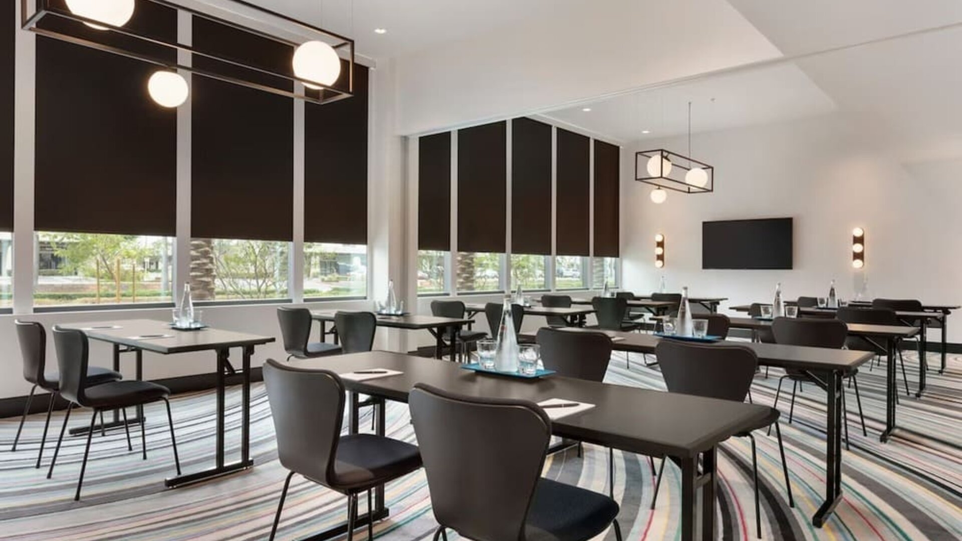 Contemporary meeting room at The Viv Hotel, Anaheim, A Tribute Portfolio Hotel featuring flexible conference-style seating, natural light, modern lighting fixtures, and presentation facilities for business meetings and events.