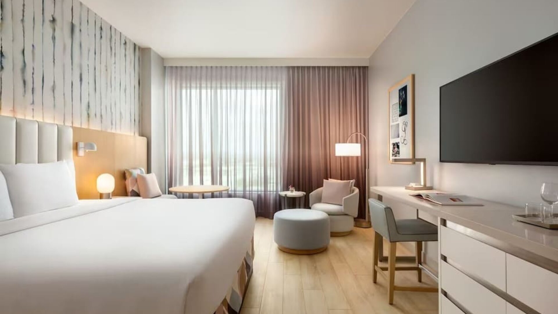 Bright king guest room with floor-to-ceiling windows, a dedicated workspace, comfortable lounge seating, and contemporary décor accented by soft pastel tones.