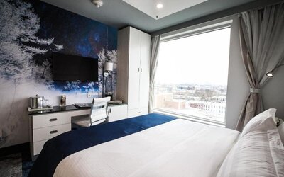 Contemporary king guest room with floor-to-ceiling windows, city views, a dedicated workspace, wall-mounted television, and modern nature-inspired décor.