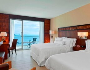 Deluxe Double Room with Ocean View, featuring two beds, a private bathroom with amenities, a safe, a desk, a telephone, ironing facilities, a tea/coffee maker, a hairdryer, a television, cable channels, and an alarm clock.